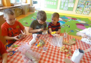 Trzech chłopców przygotowuje stroje ekologiczne z rolek papierowych i plastikowych naklejek, naklejają elemnty.